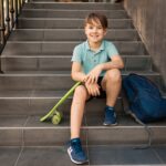 École en polo bleu assis dans les escaliers avec un sac à dos bleu et une planche verte