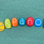 Mot Español composé de lettres en pierre multicolorées sur du sable vert